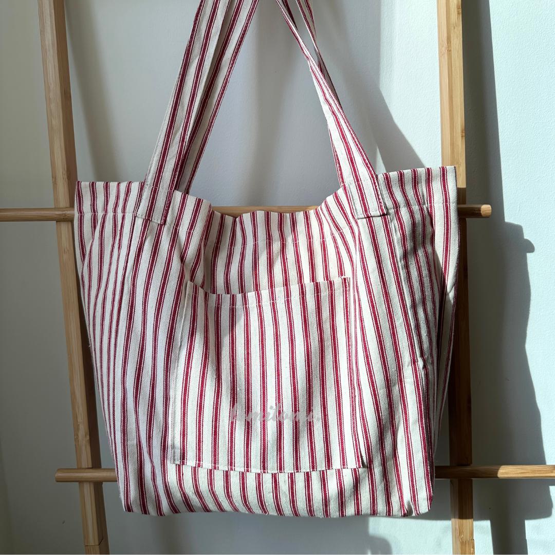 May include: A red and white striped tote bag with a single pocket on the front. The pocket has the words 'Paris, France' embroidered on it.